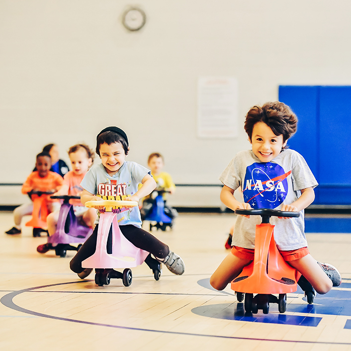 Kids on mini scooters at a gymnasium.