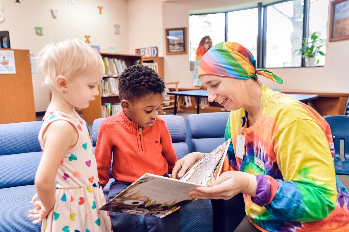 A staff member reading a book to two children.