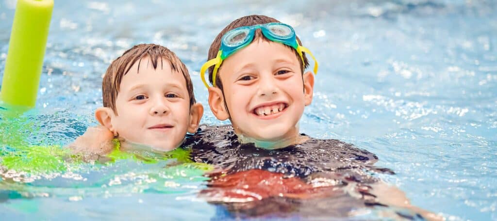 Two elementary aged boys smiling at the indoor pool